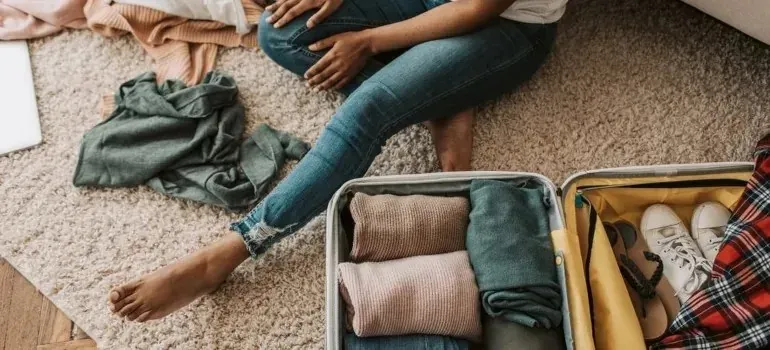 Person packing rolled clothes and sneakers into open suitcase
