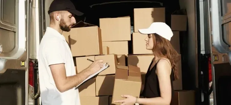 Movers with clipboard and box at van full of boxes