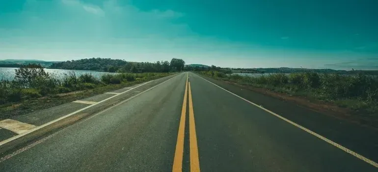 Empty two-lane highway stretching past lake and greenery
