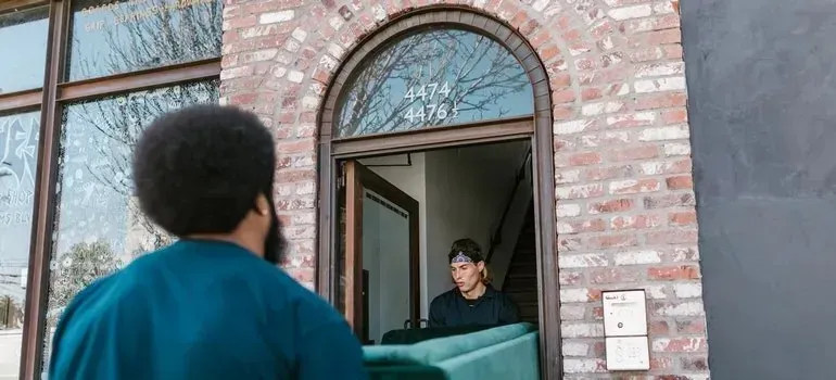 Movers carrying green sofa through brick building doorway
