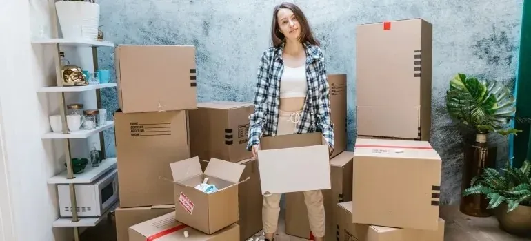 Woman in plaid shirt holding box among moving boxes