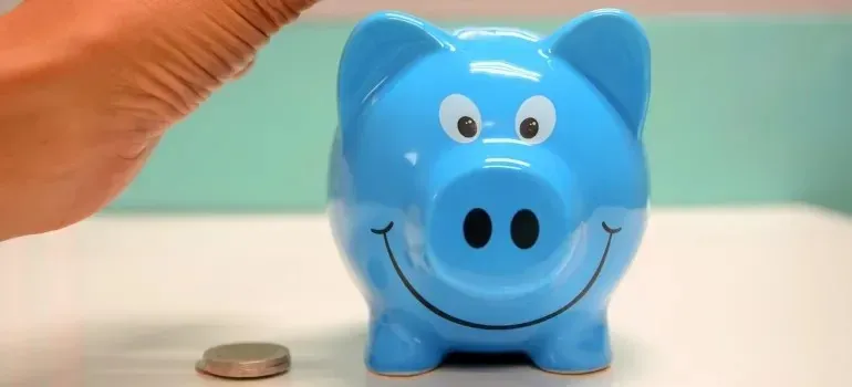 Hand dropping coin into smiling blue piggy bank