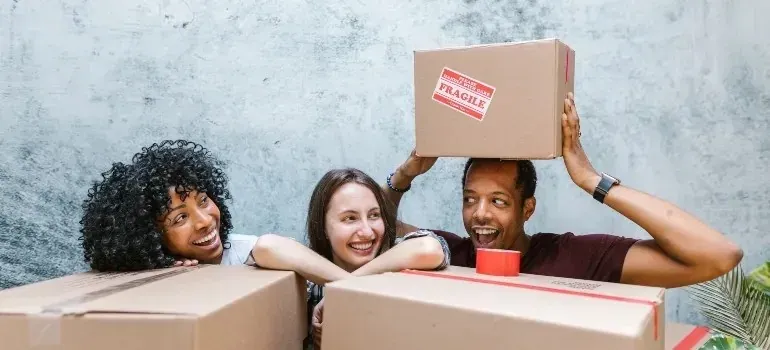 Three friends laughing, one lifting fragile-stickered box overhead