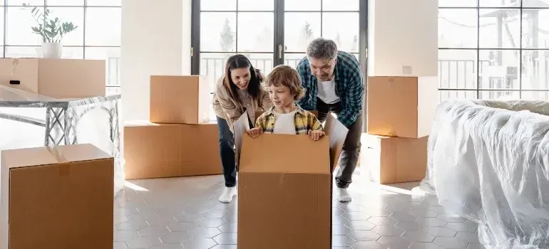 Parents playfully pushing child inside cardboard box at home