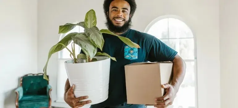 Smiling man holding potted plant and cardboard box