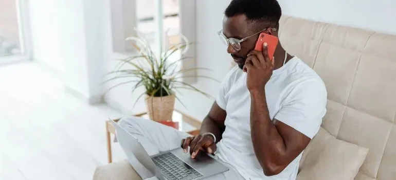 Man on couch talking on phone using laptop