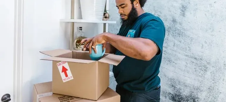 Man packing blue mug into box with caution sticker