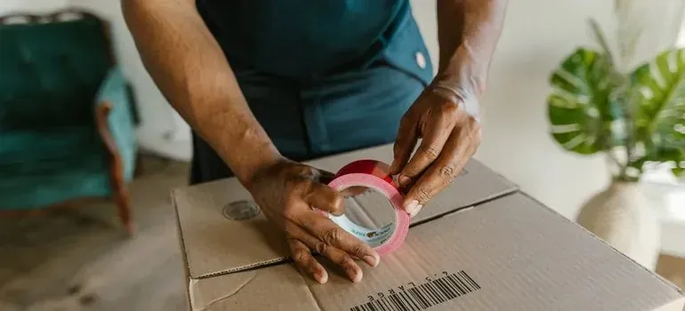 Hands taping cardboard box with red packing tape