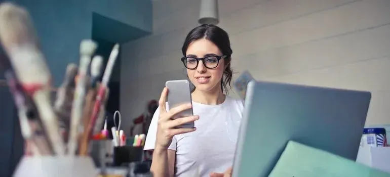 Woman in glasses reading smartphone at craft desk