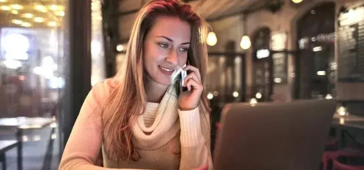Woman on phone with laptop in cozy cafe