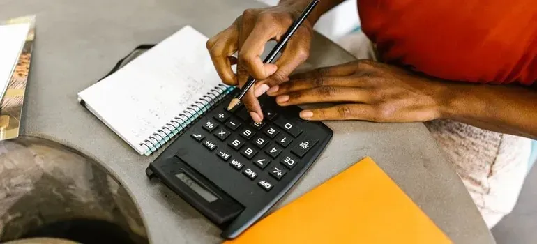 Hands using calculator with pencil, notebook, and orange folder
