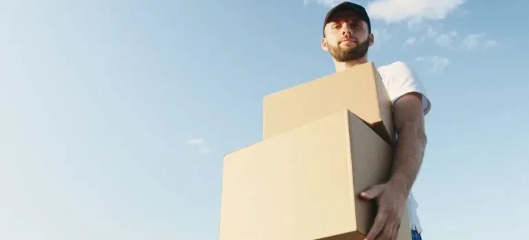 Man in cap carrying cardboard boxes under blue sky