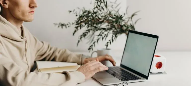 Man typing on laptop at white desk with plant