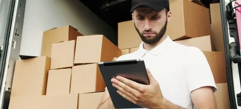 Mover in cap checking tablet inside van full of boxes