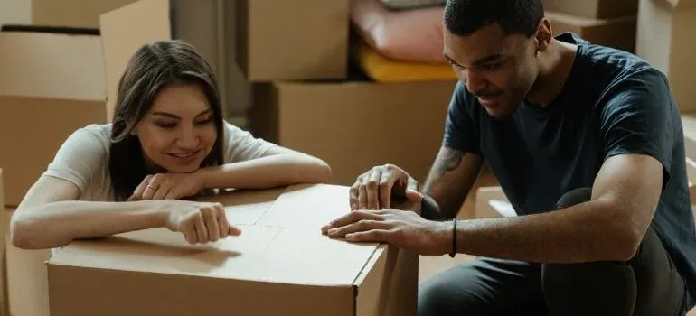Couple closing a cardboard box among moving boxes