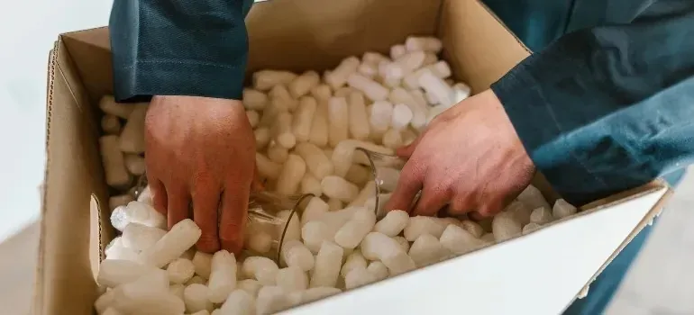Hands packing glassware into box of foam peanuts