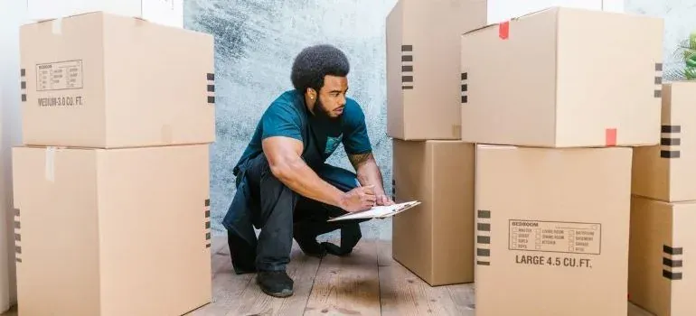 Mover with clipboard checking stacked labeled moving boxes