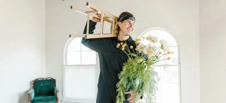 Smiling mover carrying wooden stool and flowers