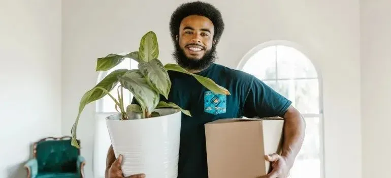 Man holding potted plant and a cardboard box