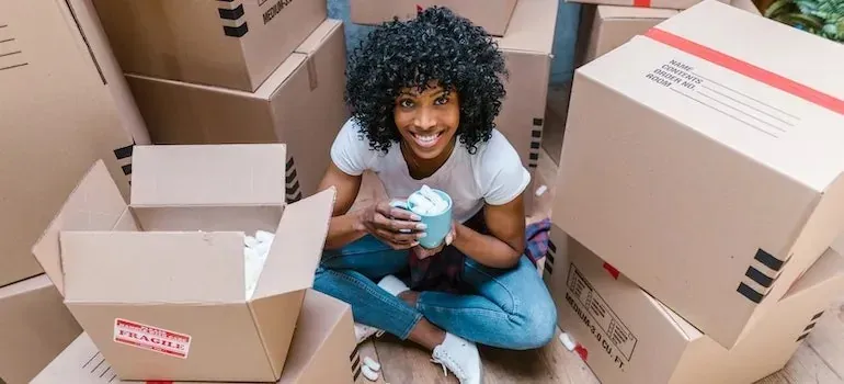 Woman with mug sitting among labeled moving boxes