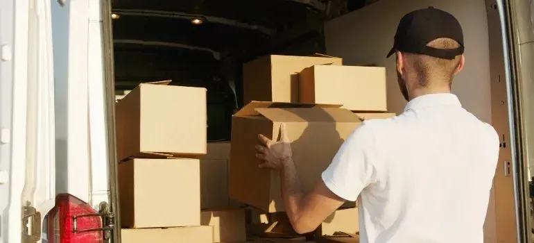 Man in white polo loading cardboard boxes into van