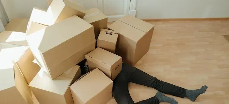 Person lying under toppled pile of moving boxes indoors