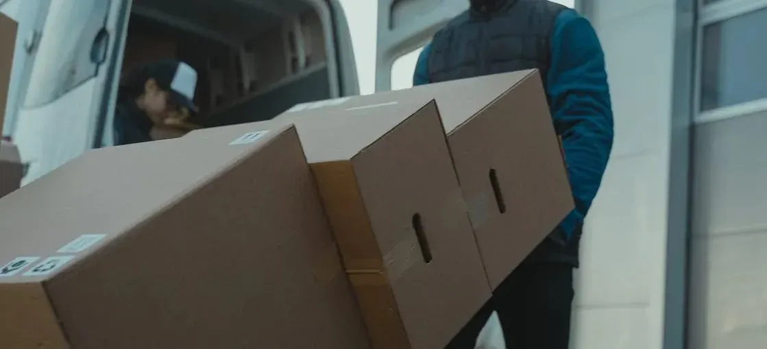 Two movers carrying long cardboard boxes out of van