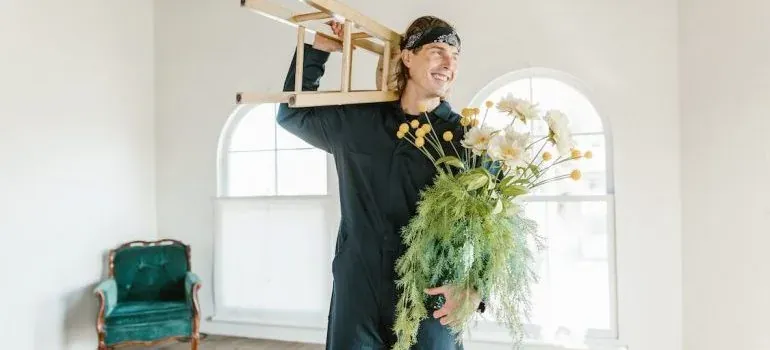 Smiling man in coveralls holding stool and flower bouquet