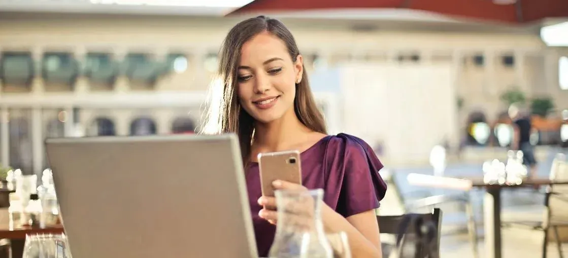 Woman using phone and laptop at outdoor cafe