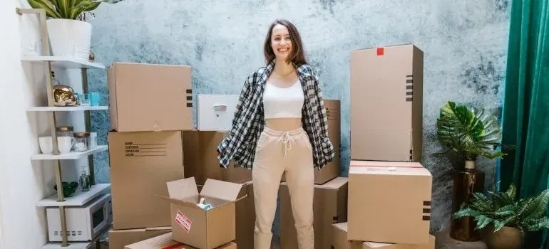 Woman standing among stacked moving boxes and houseplants
