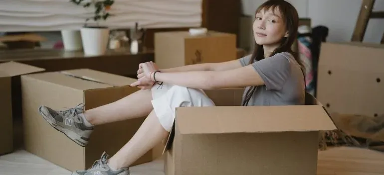 Young woman sitting inside cardboard box while unpacking