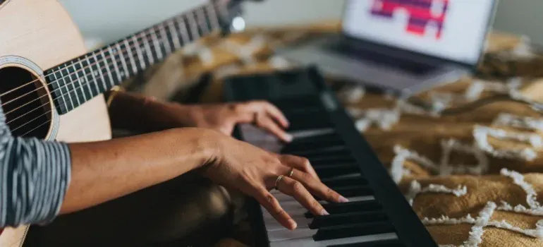 Hands playing keyboard with guitar, laptop