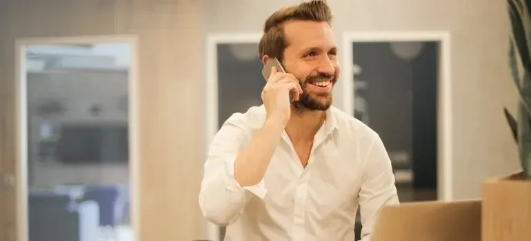 Smiling bearded man in white shirt talking on phone in office