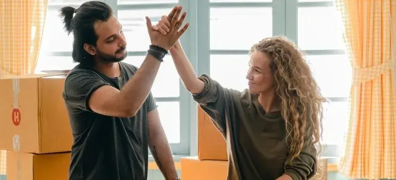 Couple high-fiving beside stacked moving boxes by windows