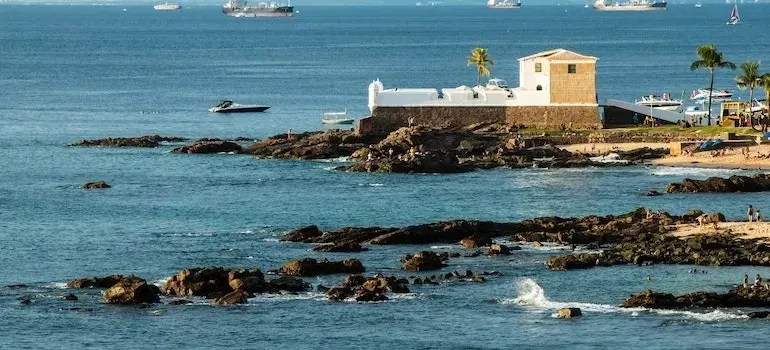 Seaside fort on rocky coast with boats and palms