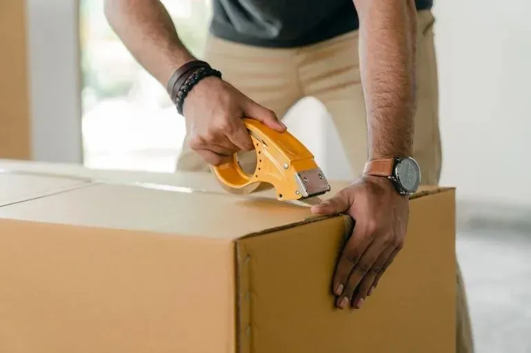 Hands sealing large cardboard box with yellow tape dispenser