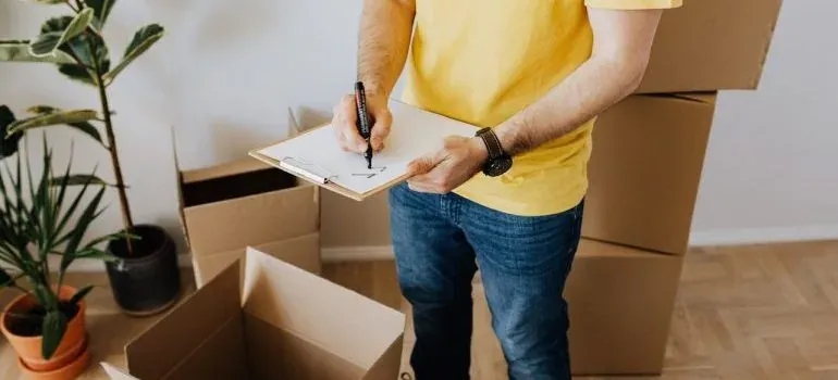 Man writing on clipboard beside open moving boxes