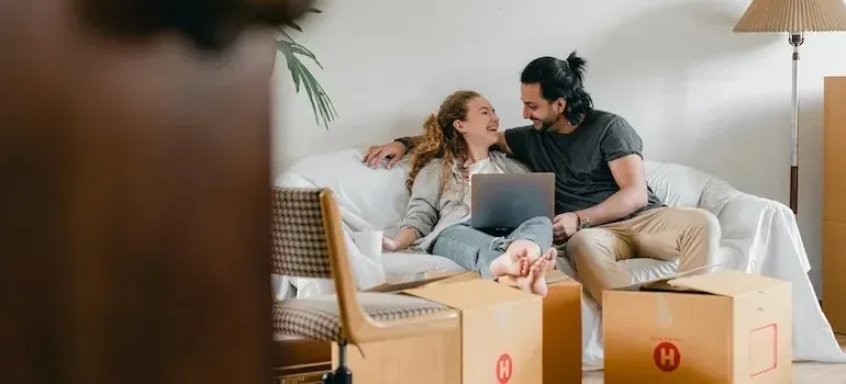 Couple relaxing on sofa with laptop among moving boxes