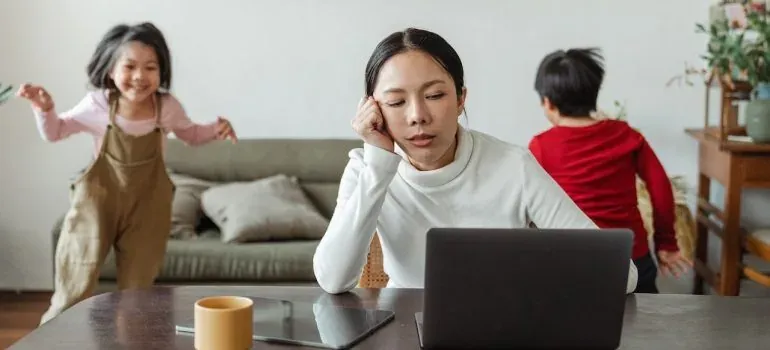 Tired mother at laptop, kids playing