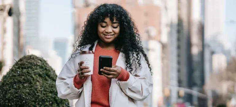 Woman with coffee using phone outdoors