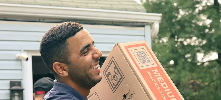 Smiling mover carrying cardboard box outside house