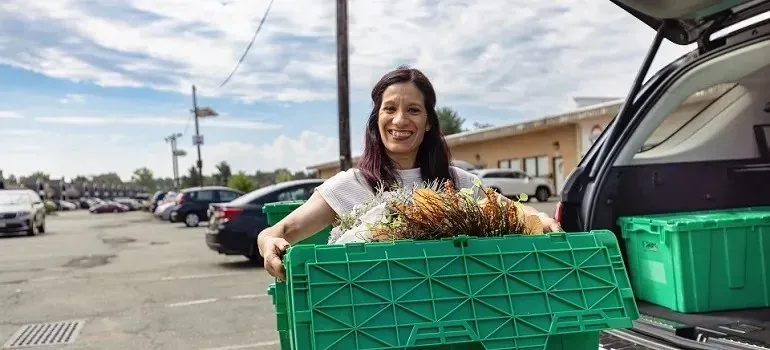 Smiling woman loading green plastic moving bins into SUV