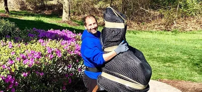 Mover carrying blanket-wrapped furniture past blooming azalea garden