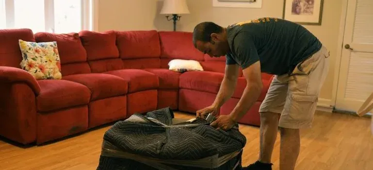 Mover wrapping ottoman in living room, red sofa