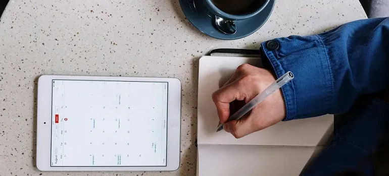 Hand writing notes beside tablet calendar
