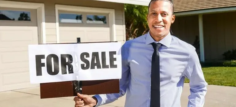 Man holding For Sale sign outside house