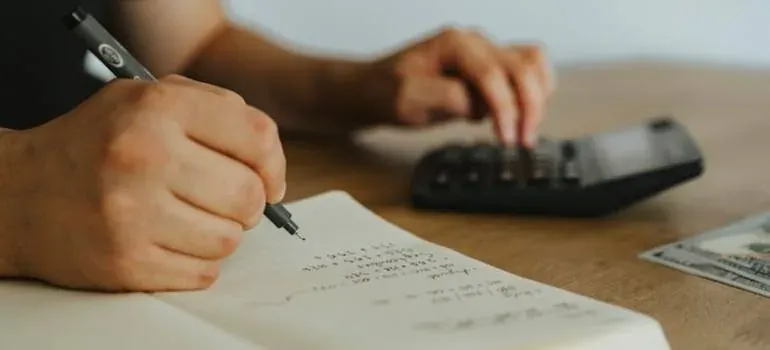 Hands writing budget with calculator