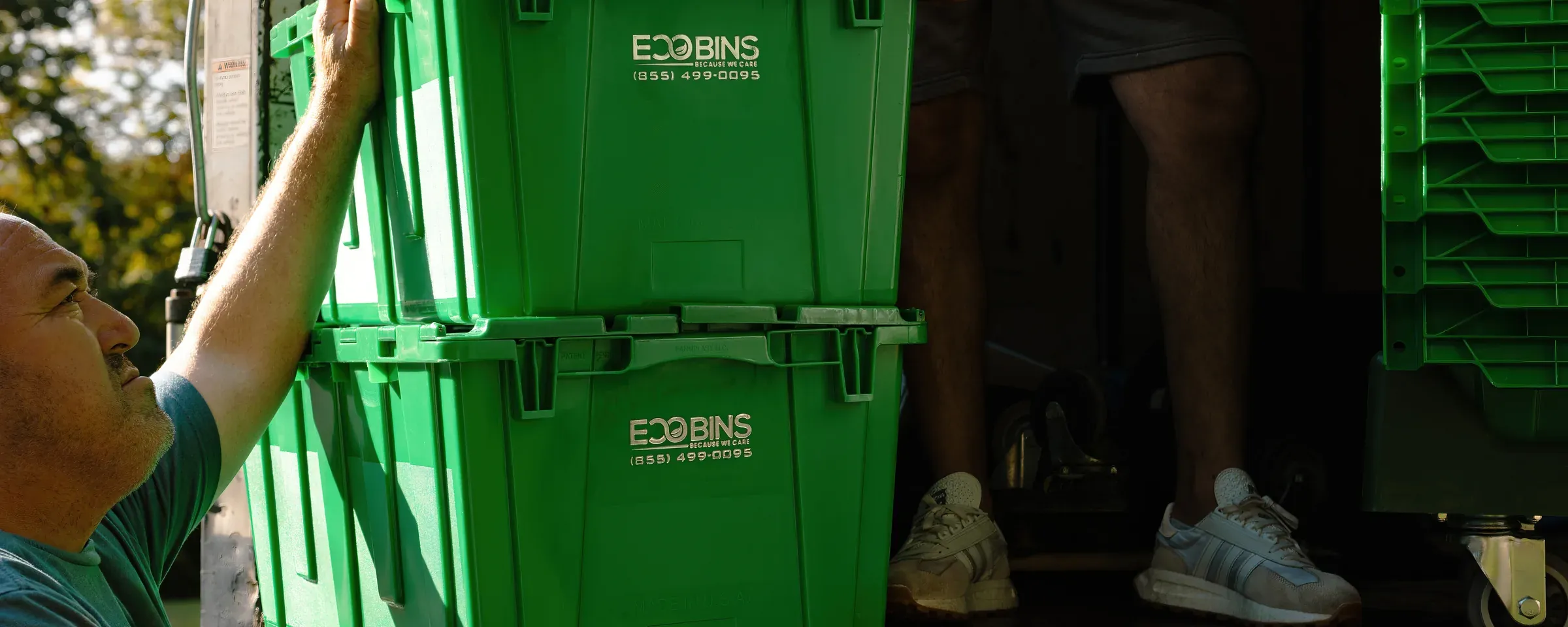 A Teddy Bear Moving crew member loading stacked green EcoBins bins into the truck