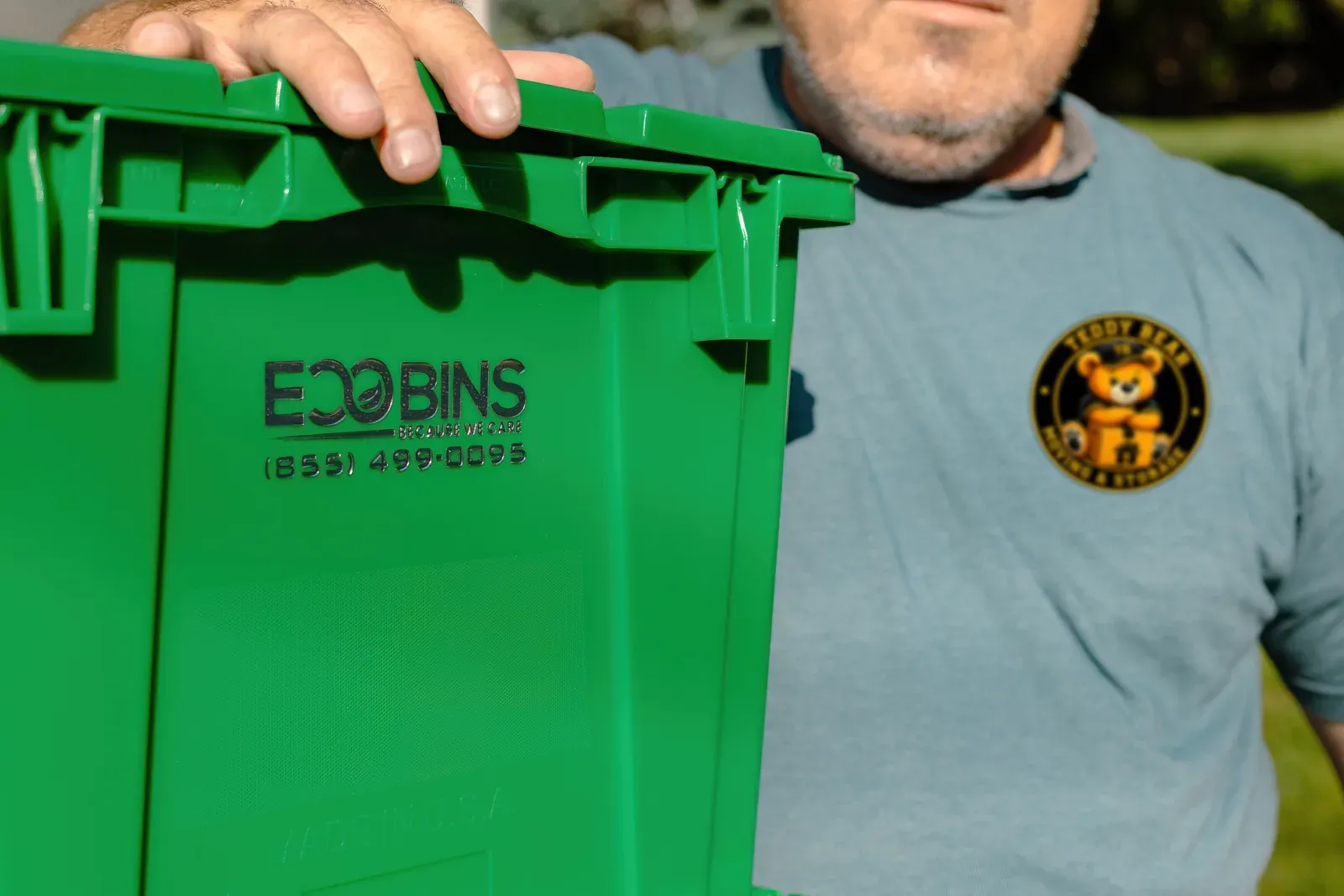 A green EcoBins bin, with the Teddy Bear Moving logo on the crew member's shirt