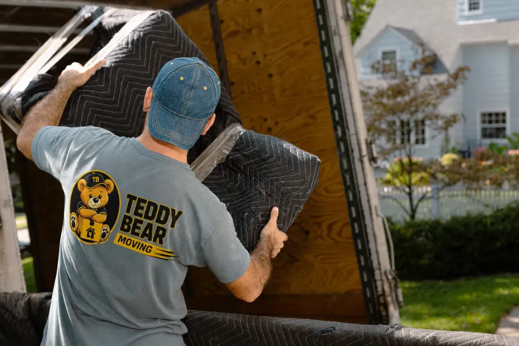 Mover in a Teddy Bear shirt carrying a furniture piece covered with moving blankets